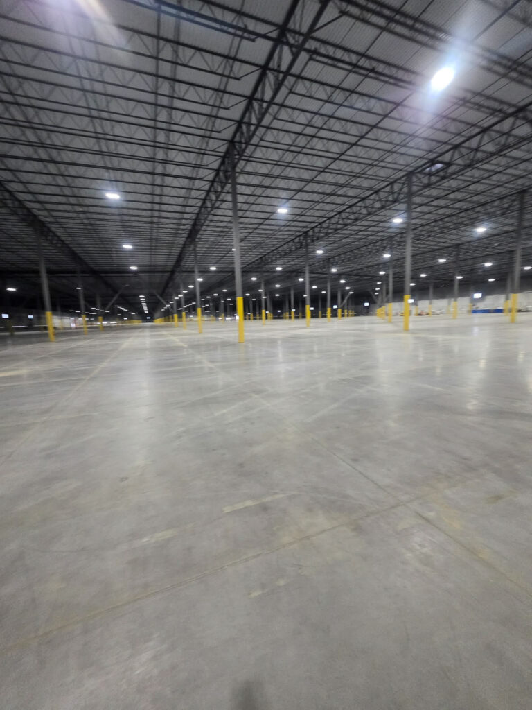 Wide concrete floor inside a warehouse with steel roof framing"