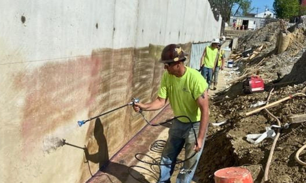 Worker applying a coating along a concrete foundation wall below grade.