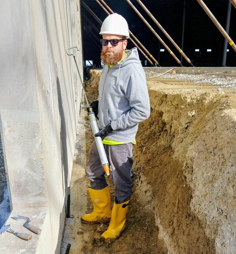 Worker with a caulking gun beside a foundation wall"