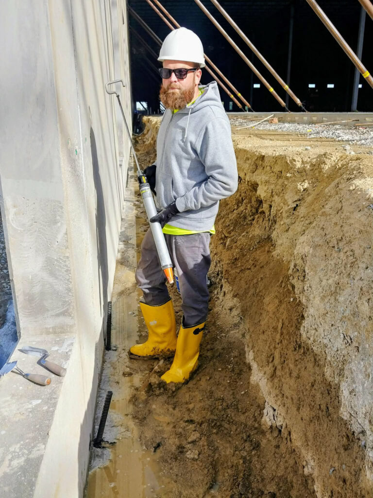 Worker with a caulking gun beside a foundation wall"