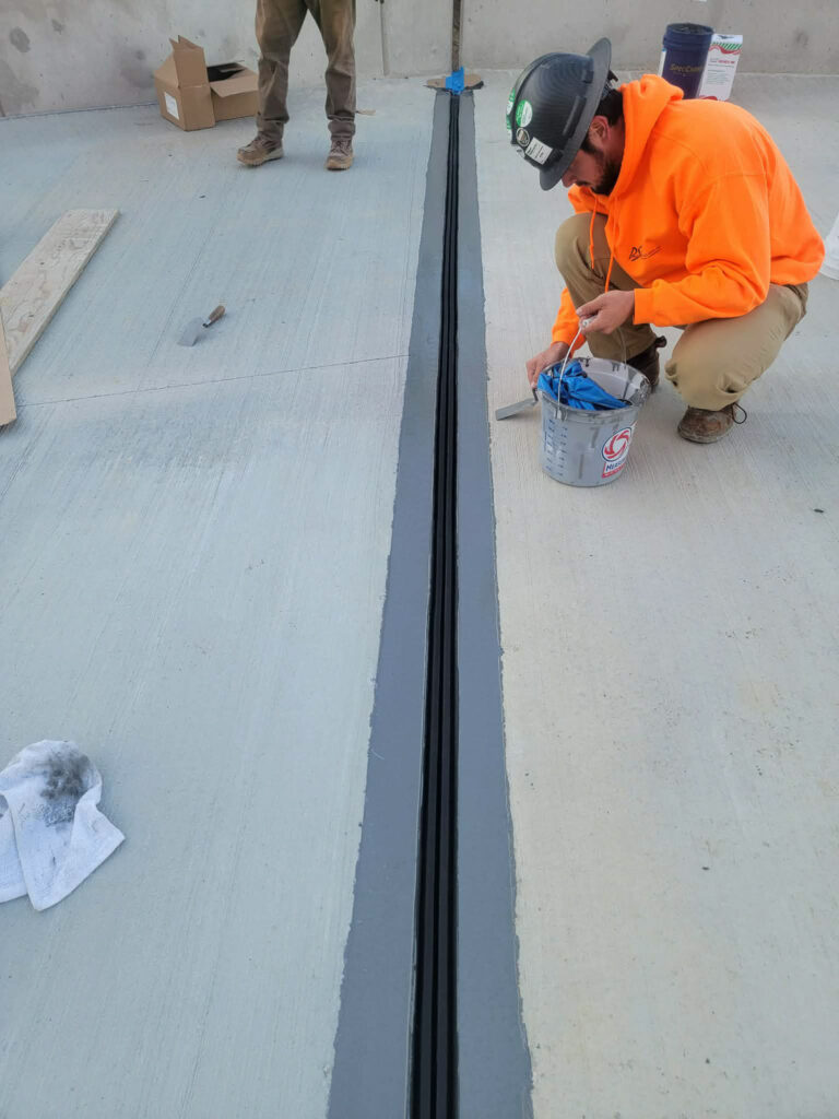 Worker applying material beside an open joint on a concrete deck"