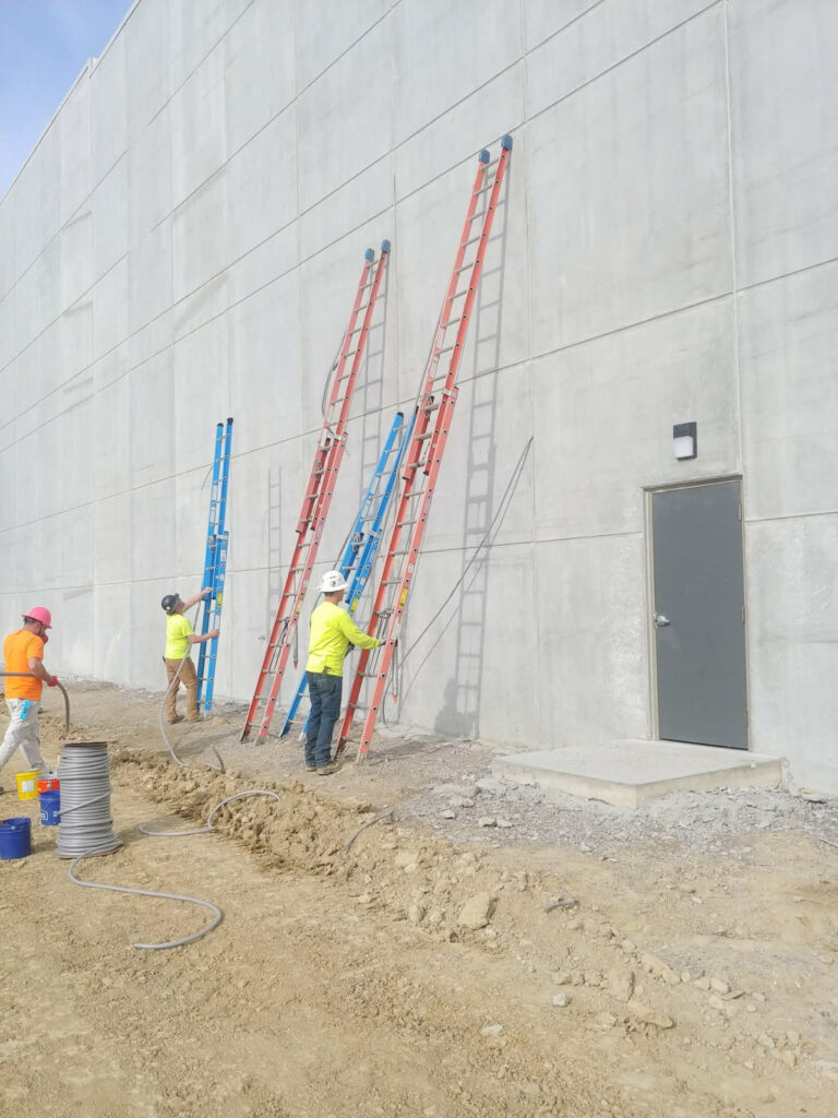 PSI field crew at a large commercial concrete wall with ladders and access equipment.