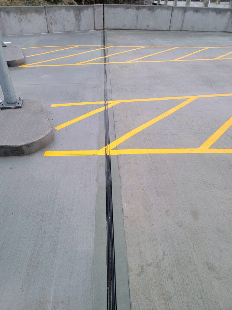 Expansion-joint profile crossing a parking deck with yellow traffic markings"