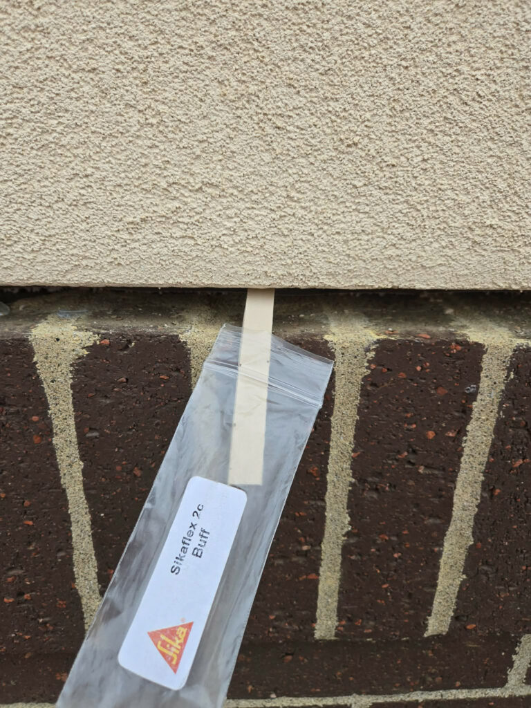 Sikaflex 2c Buff sealant sample held against brickwork and masonry"